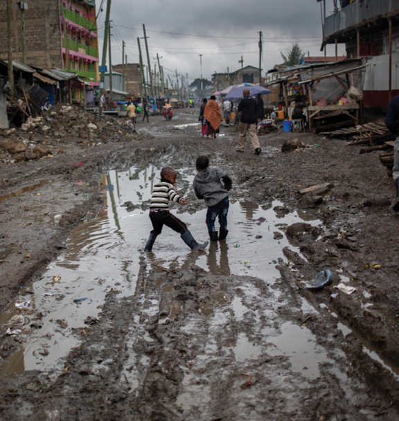 Girls in wellington boots dance in a puddle in the street in Mukuru Kwa Njenga, Nairobi, Kenya 