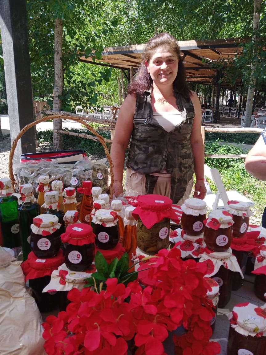 A woman stands behind a table filled with products like jams