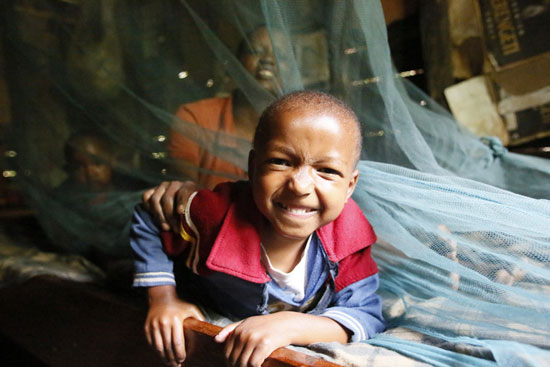 smiling boy sticks his head out from under bed net