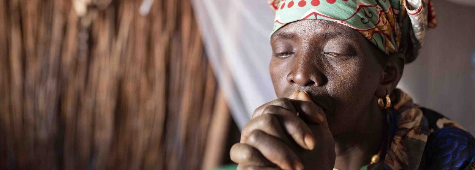 A woman appears to be praying, with her hands folded in front of her face.