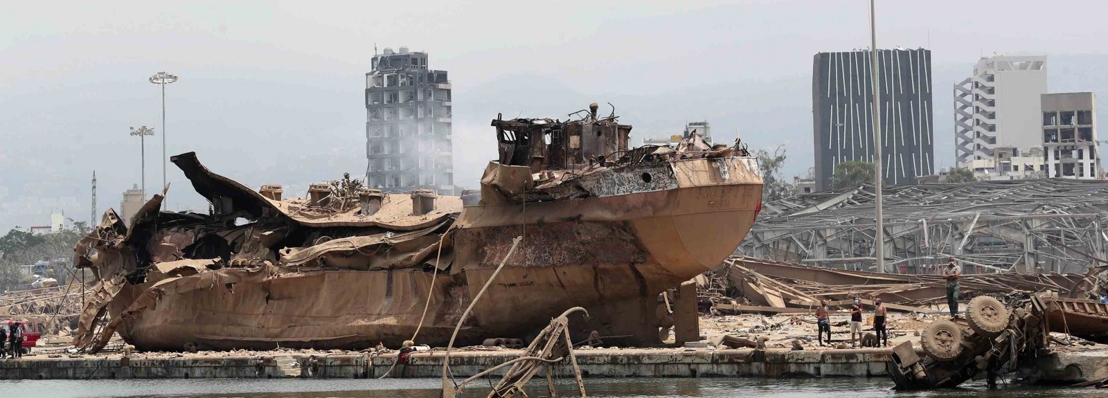 People stand by the wreckage of a ship at the devastated site of the explosion in the port of Beirut, Lebanon, Thursday Aug.6, 2020. (AP Photo/Thibault Camus, Pool)