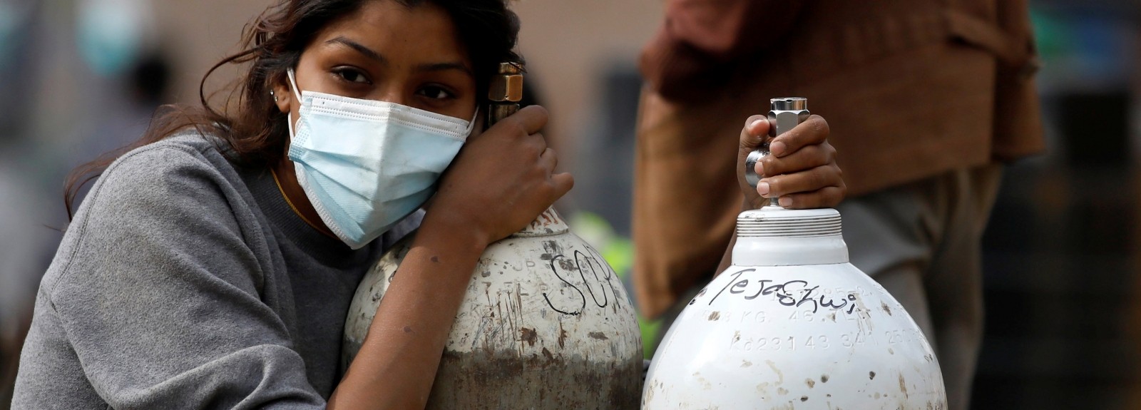 A woman wearing a face is leaning on an oxygen tank.