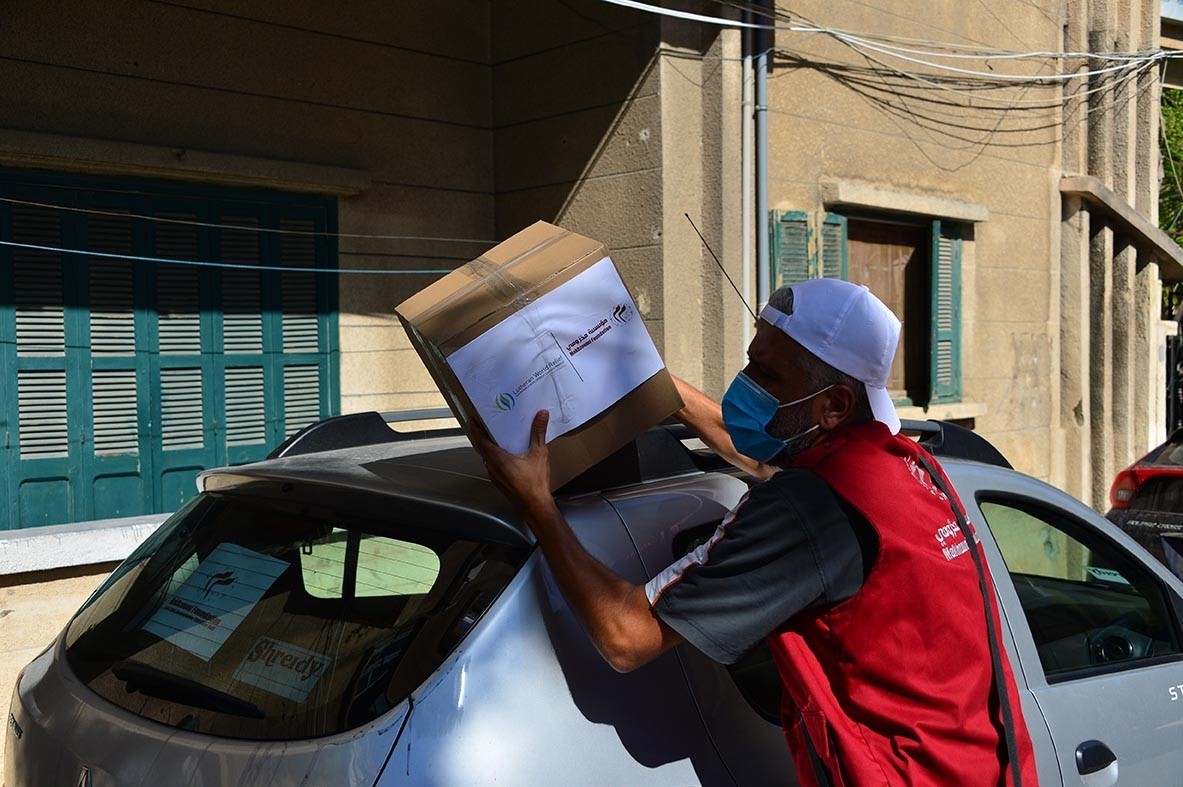 Food parcels in brown boxes are loaded in the cars of waiting volunteers.