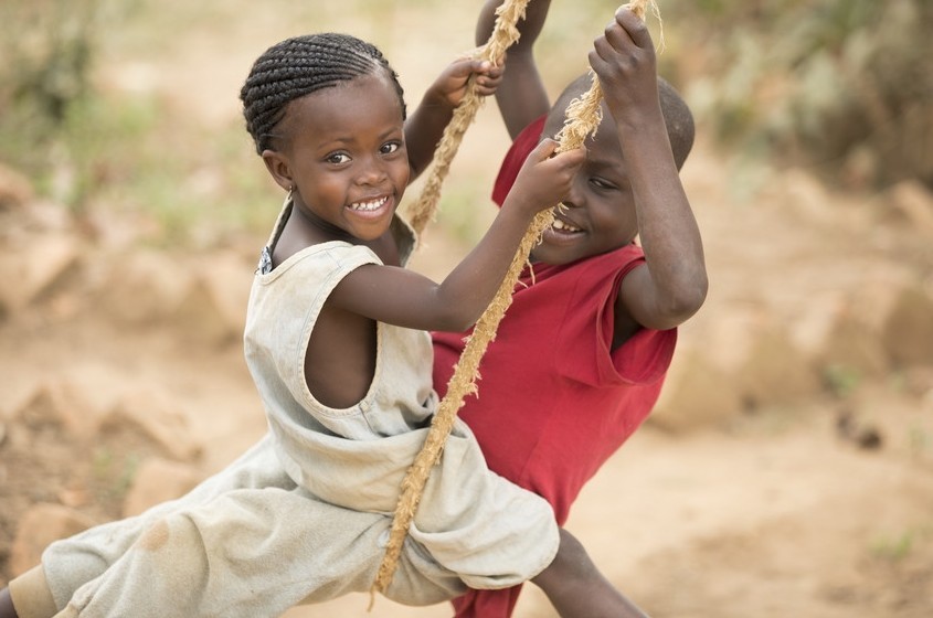 Two children smile while on a rope swing.