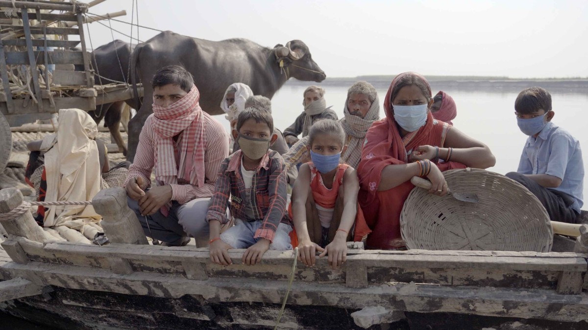 Children and adults, who are all wearing face coverings, are seated in a wooden boat.