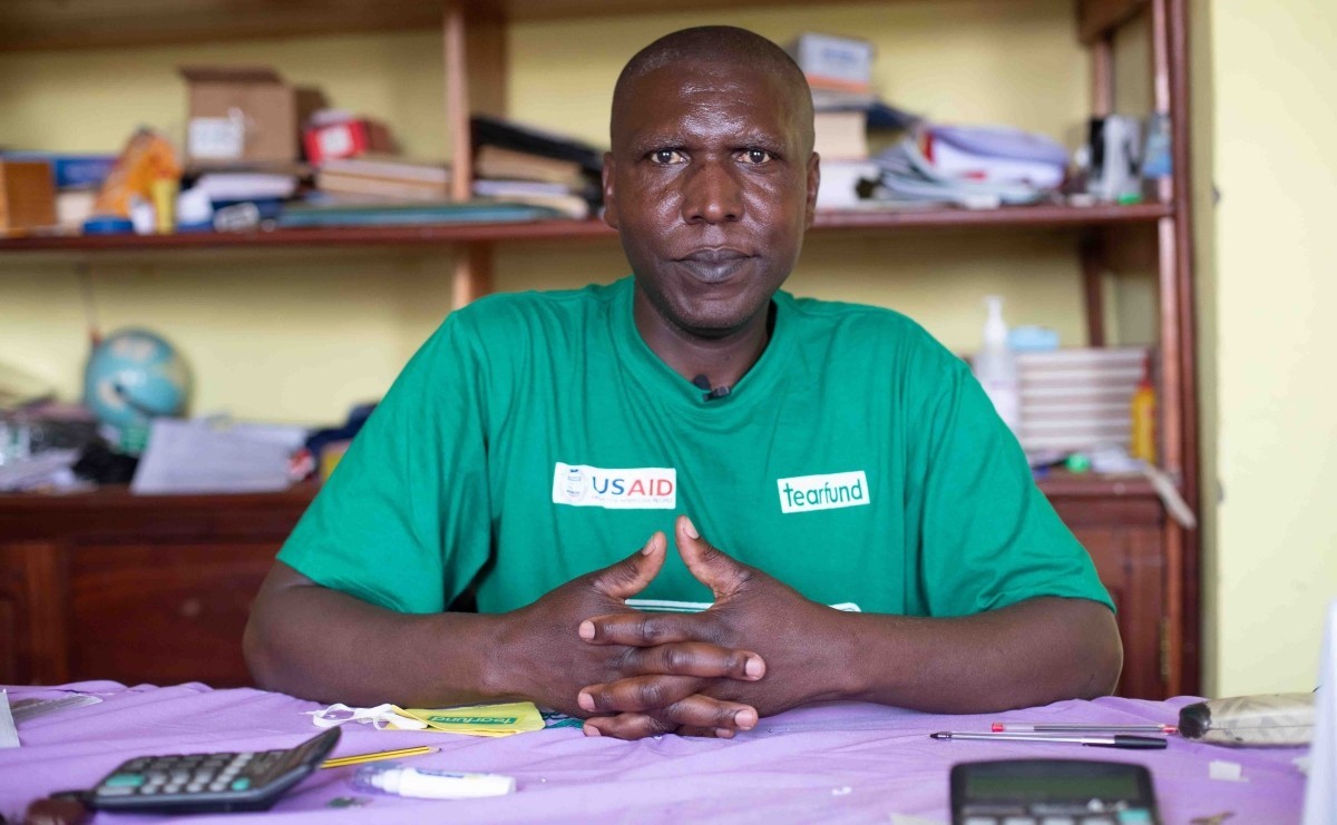 A man in a green shirt looks at the camera. His name is Emmanuel Kasereka Sikuli, and he is a school headmaster in Butembo in the Democratic Republic of Congo.