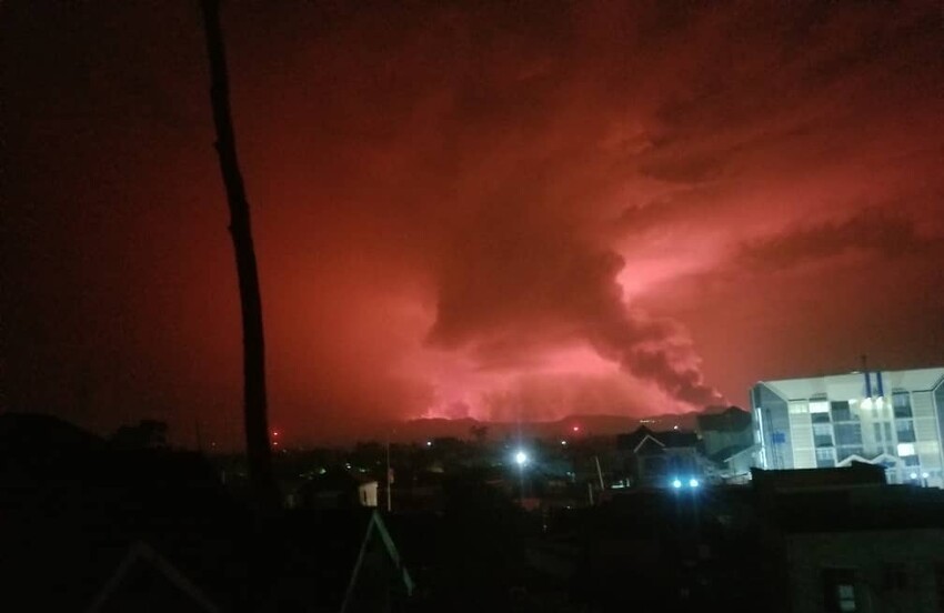 Smoke from a volcano can be seen in a reddish sky.