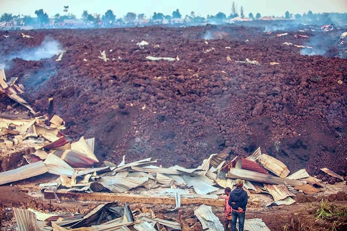 A wave of cooled lava sits on top of damaged structures.