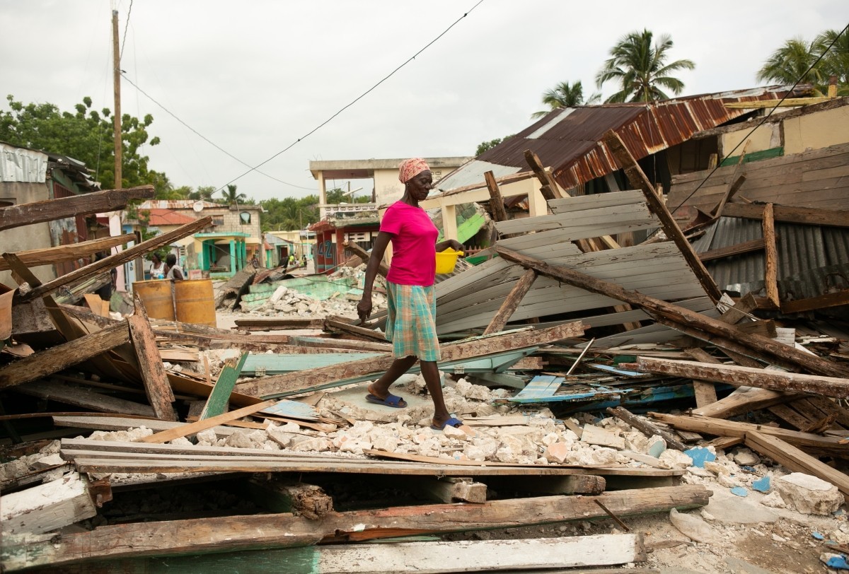 A Haitian woman in a pink shirt walks over rubble left behind by the earthquake.