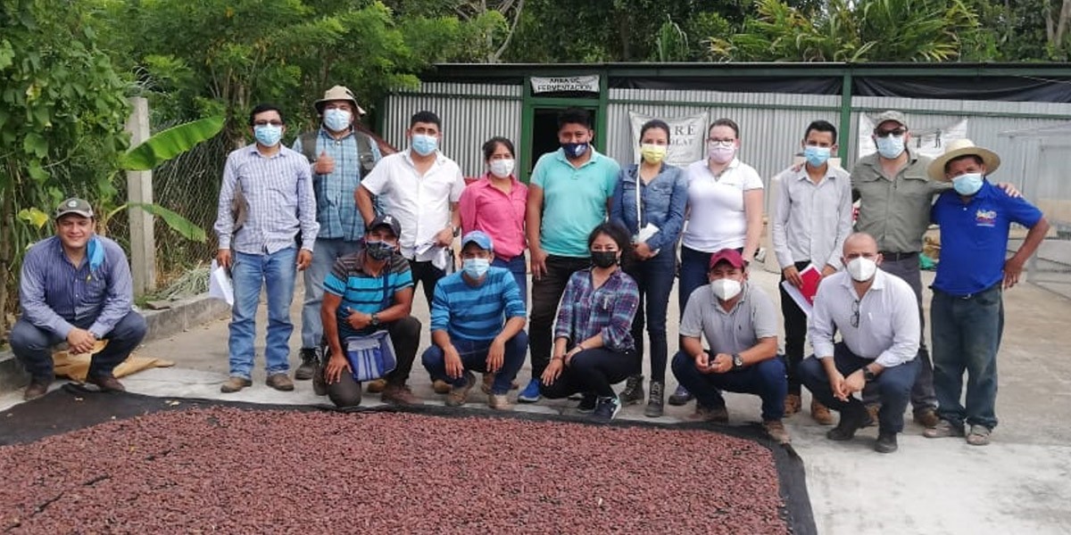 Students gather together wearing masks behind a tarp covered with cocoa beans