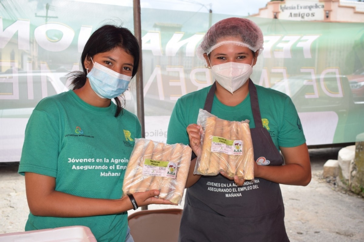Two youth in green t-shirts and wearing masks are holding packaged food