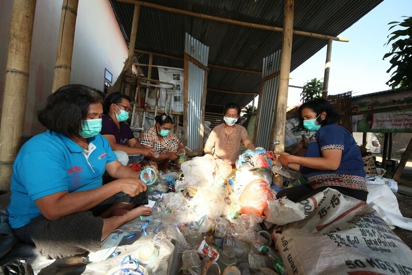 A group of women wearing masks sit in a semi-circle sorting plastic waste