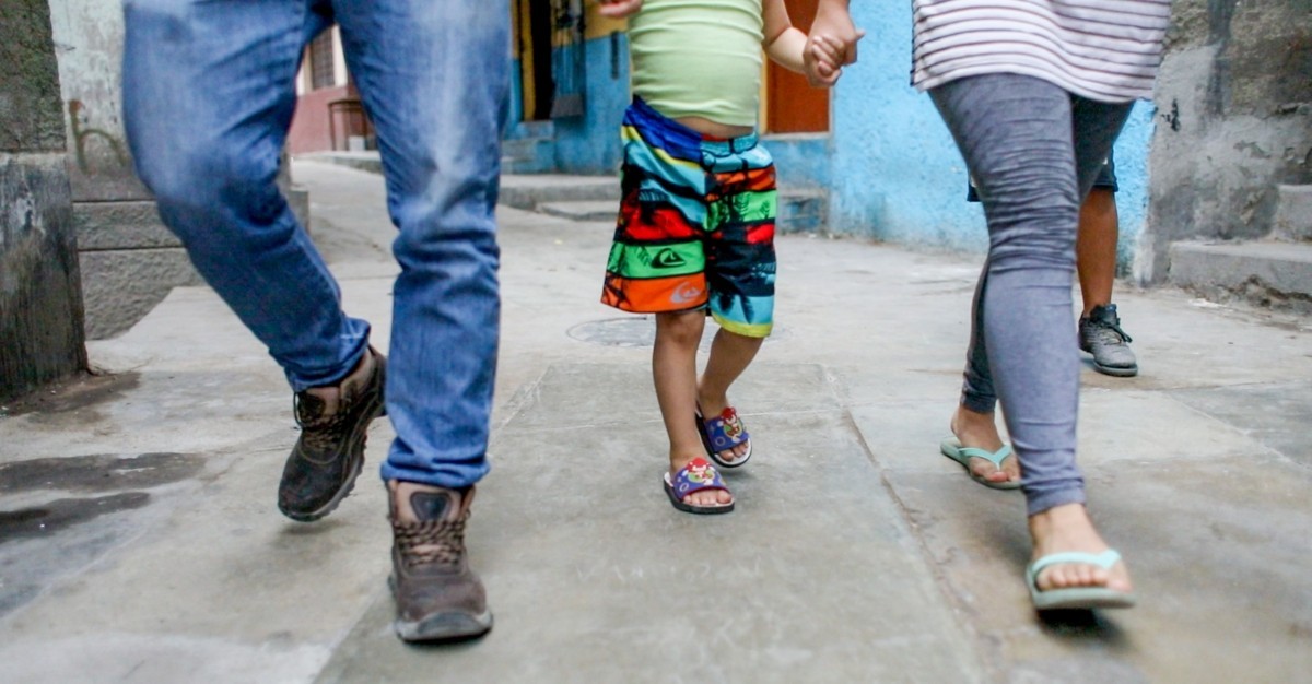 The legs of a man, child and woman are shown as they walk on a narrow street