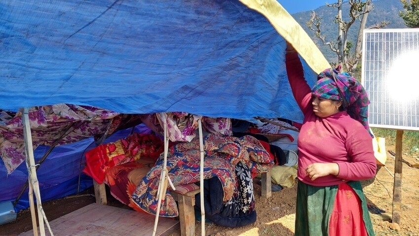 A woman lifts a tarp to show her belongings underneath