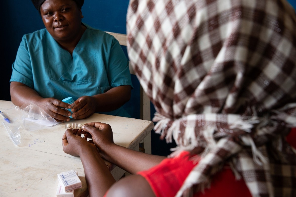 A woman wearing a head scarf holds medicine in her hands
