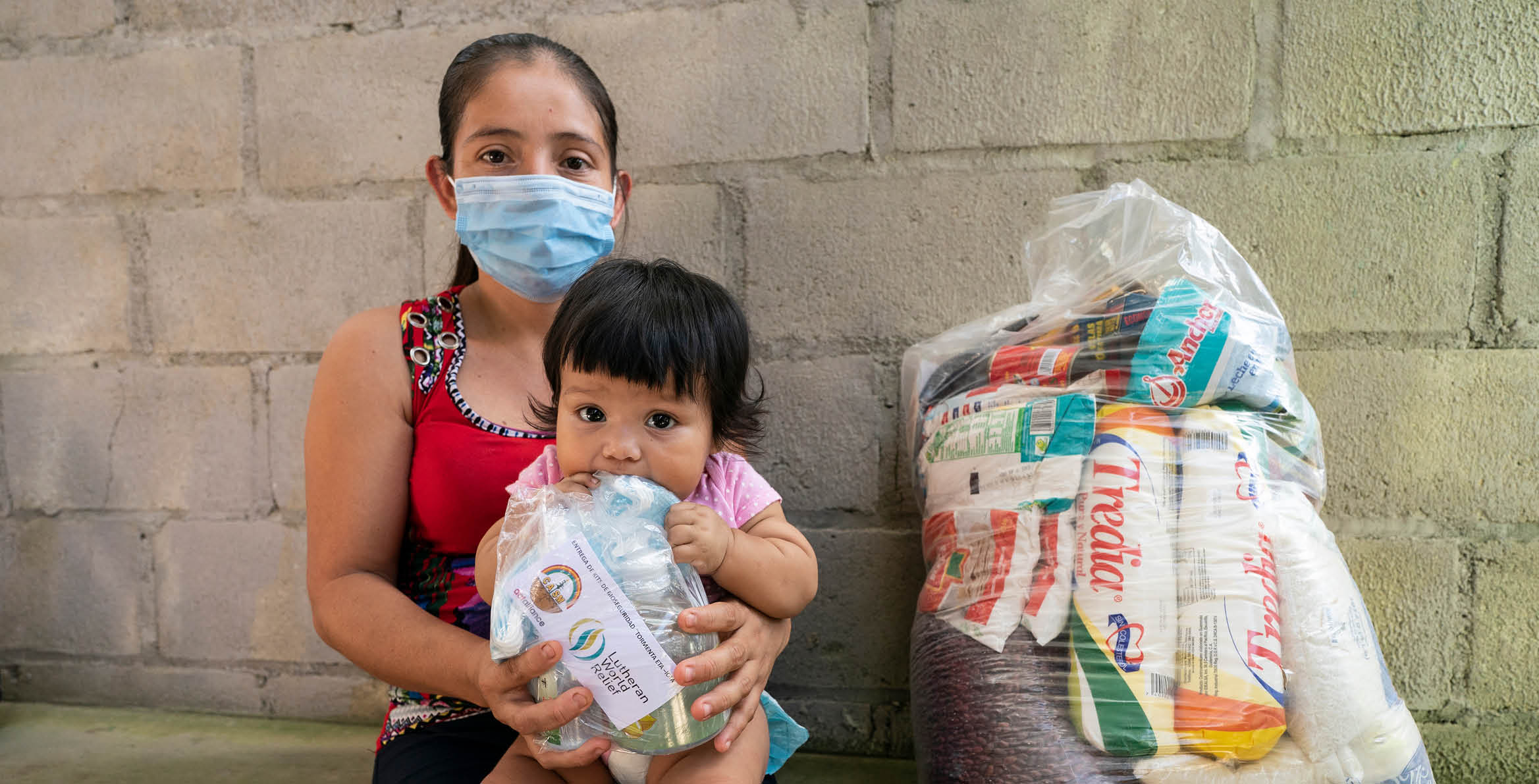 Elsa Marina Amaya holds her six-month-old daughter Rosa Linda at the Lutheran World Relief aid distribution to 137 families in Waller Bordo, a community near Choloma, Honduras  This community, which sits between the Chamelecon and Ulua Rivers, was devastated when both rivers breached levees protecting the community during Hurricanes Eta and Iota in November 2020   Prior to the COVID outbreak and the hurricanes, she worked in kitchens to support herself and her three daughters ages 9, 3, and six months  This 30-year-old mother says she needs food, diapers, milk, medicines, and vitamins for her children   The aid distribution will provide six weeks of food  She says its a relief and a blessing because she has no income source at this time 