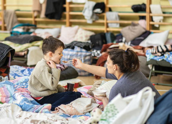 In a converted school gymnasium in the small town of Przemysl in Poland near the border with Ukraine, Ukrainian refugees are given food, clothing, and a place to sleep temporarily while they plan their journey to more stable lodgings  In less than three weeks after war in Ukraine began, more than 2 7 million Ukrainians—mostly mothers and children, because men age 18 to 60 are required to stay in Ukraine—fled to Poland to escape bombs and bullets in their hometowns  Many are moving onward to other European countries like Germany and Italy 