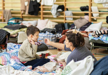 In a converted school gymnasium in the small town of Przemysl in Poland near the border with Ukraine, Ukrainian refugees are given food, clothing, and a place to sleep temporarily while they plan their journey to more stable lodgings  In less than three weeks after war in Ukraine began, more than 2 7 million Ukrainians—mostly mothers and children, because men age 18 to 60 are required to stay in Ukraine—fled to Poland to escape bombs and bullets in their hometowns  Many are moving onward to other European countries like Germany and Italy 